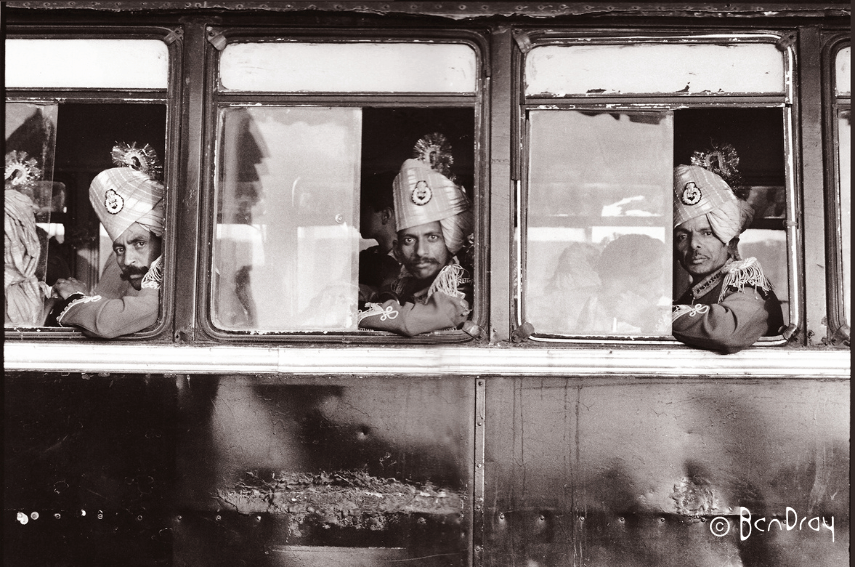 Three men wearing headwear who are part of a military band on a bus waiting to leave the Jaisalmer Festival in India.