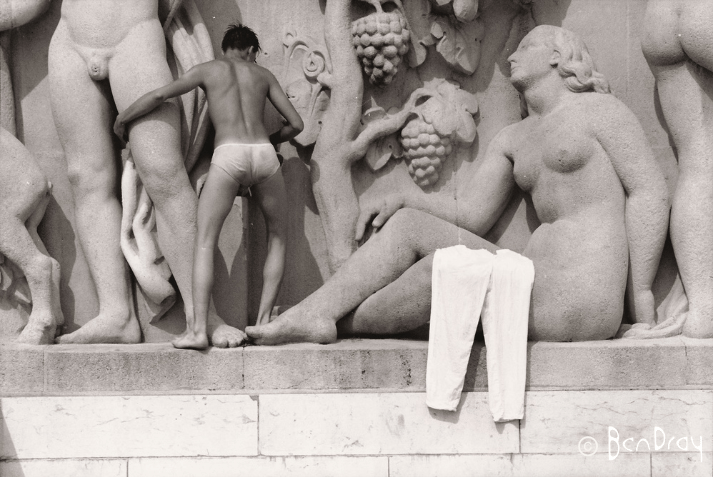 A man climbs over the fountain in the Paris Statues Jardins du Trocadéro, Paris. Trousers are draped over the leg of one of the statues.