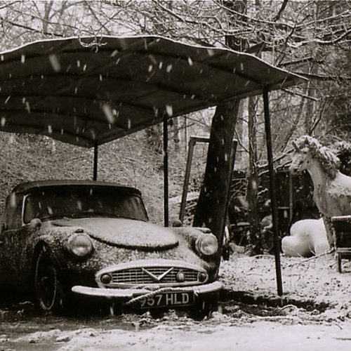 A vintage Daimler Dart car and prop unicorn in the snow surrounded by trees.