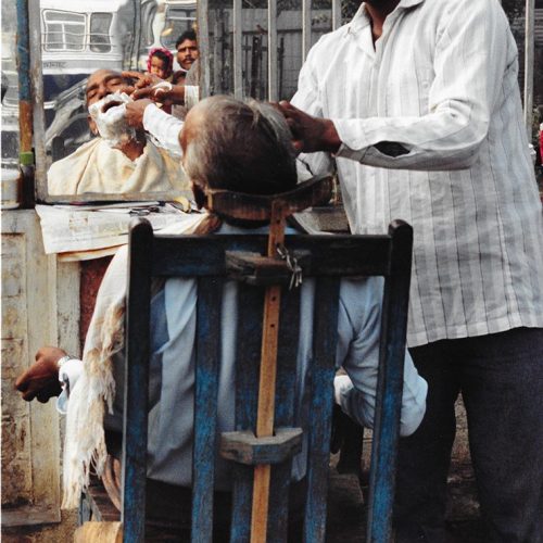 A man is shaved and reflected in a mirror in a Delhi bus depot
