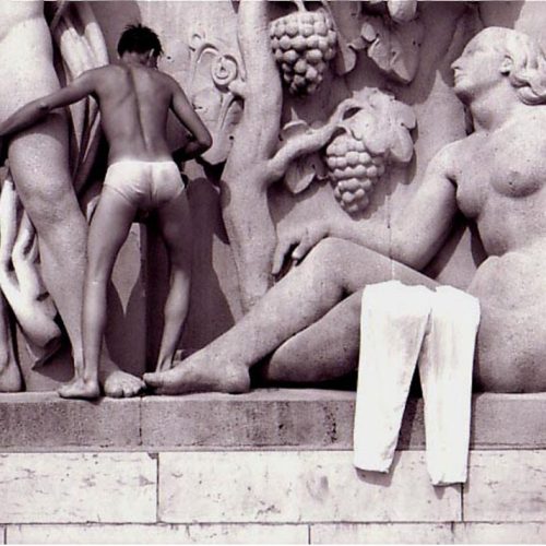 a naked man climbs across neo classical statues in Trocadero Square near fountain and Eiffel Tower Paris