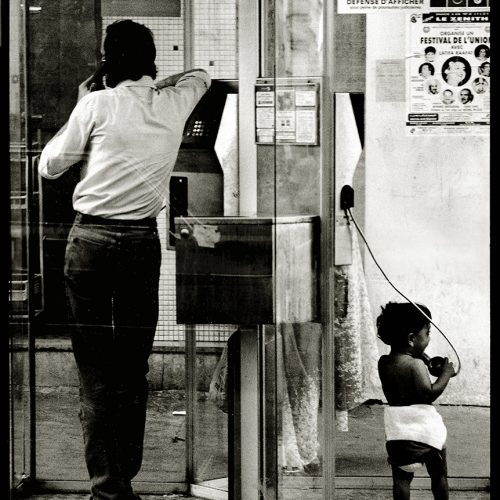 a phone box in a Parisian street with a man on one side and a small child on the other