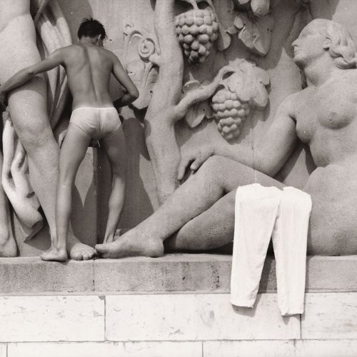 Black and white image of a semi naked man climbing across a frieze of statues.